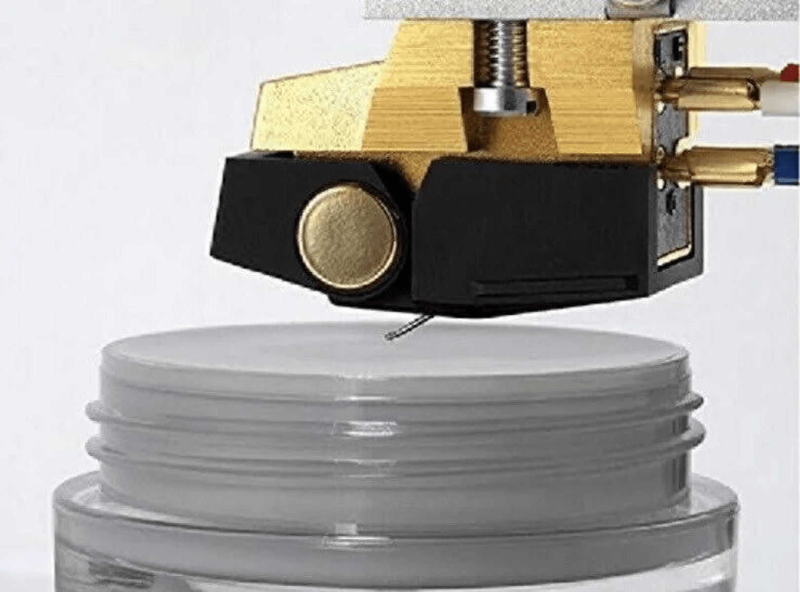Primer plano de una cápsula de tocadiscos sobre una tapa blanca, mostrando la aguja y el cuerpo dorado y negro.