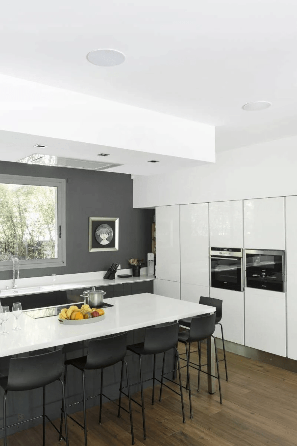 Moderna cocina con isla blanca, taburetes negros, pared de acento oscura y hornos empotrados.