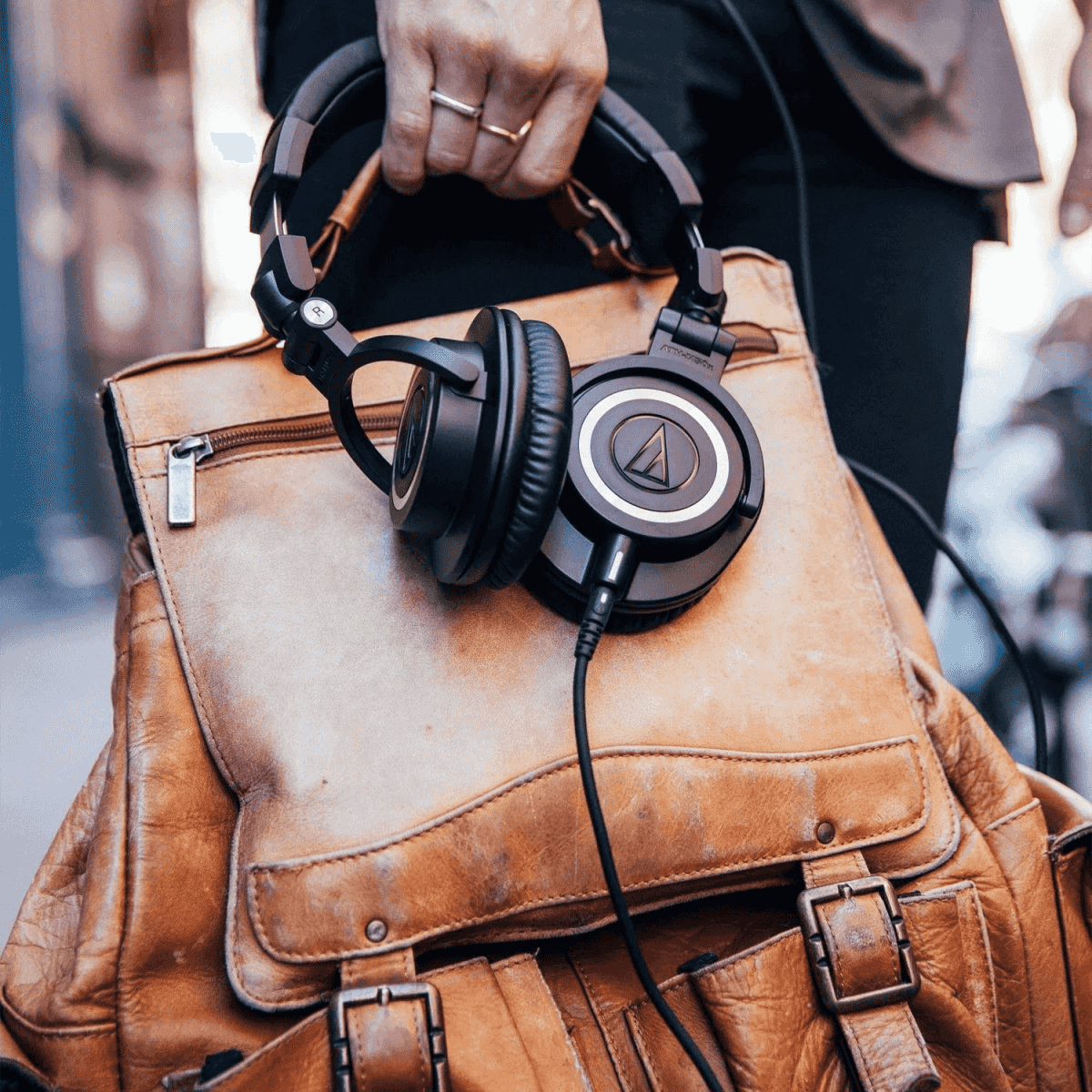 Persona sosteniendo una mochila de cuero marrón y auriculares negros.
