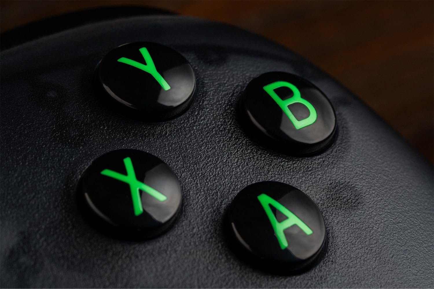 Zblizenie czterech czarnych przyciskow kontrolera Xbox z swiecacymi na zielono literami Y, B, X i A.