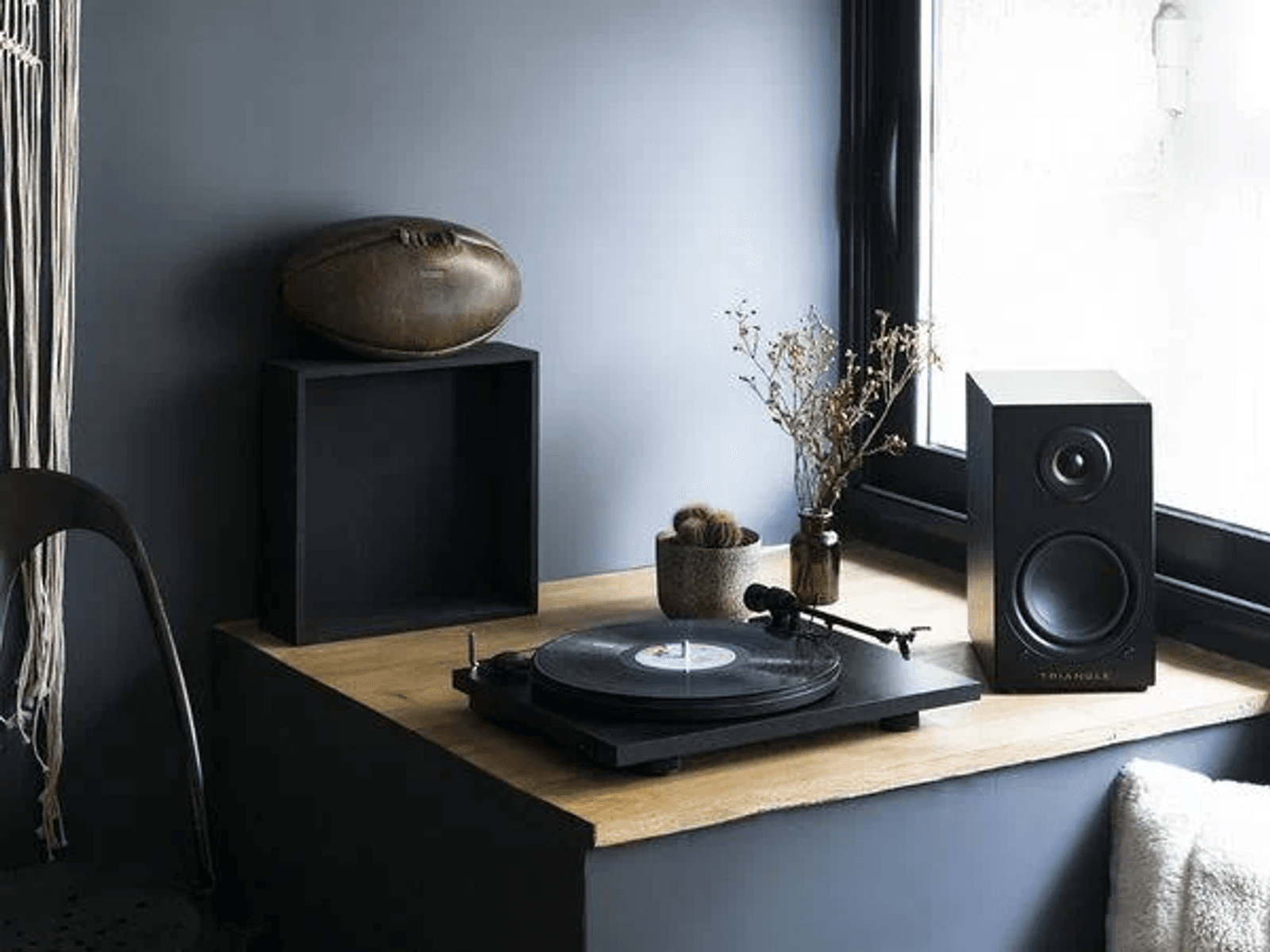 Un tocadiscos, un altavoz y decoración en una mesa de madera contra una pared azul.
