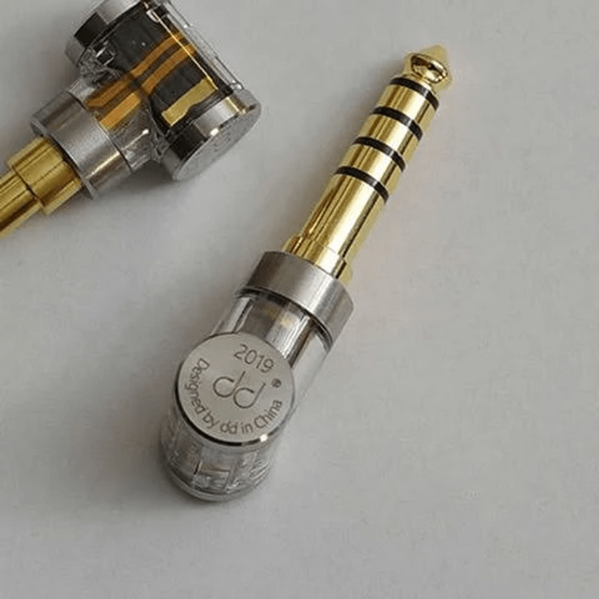 Dos conectores de audio chapados en oro con carcasas transparentes sobre fondo blanco.