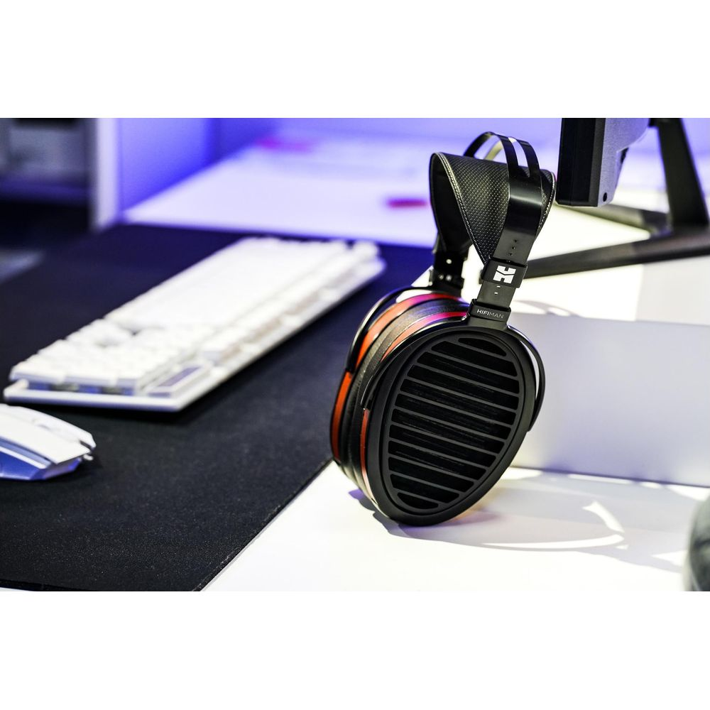 Auriculares Hifiman negros y rojos en un escritorio blanco con teclado de fondo.