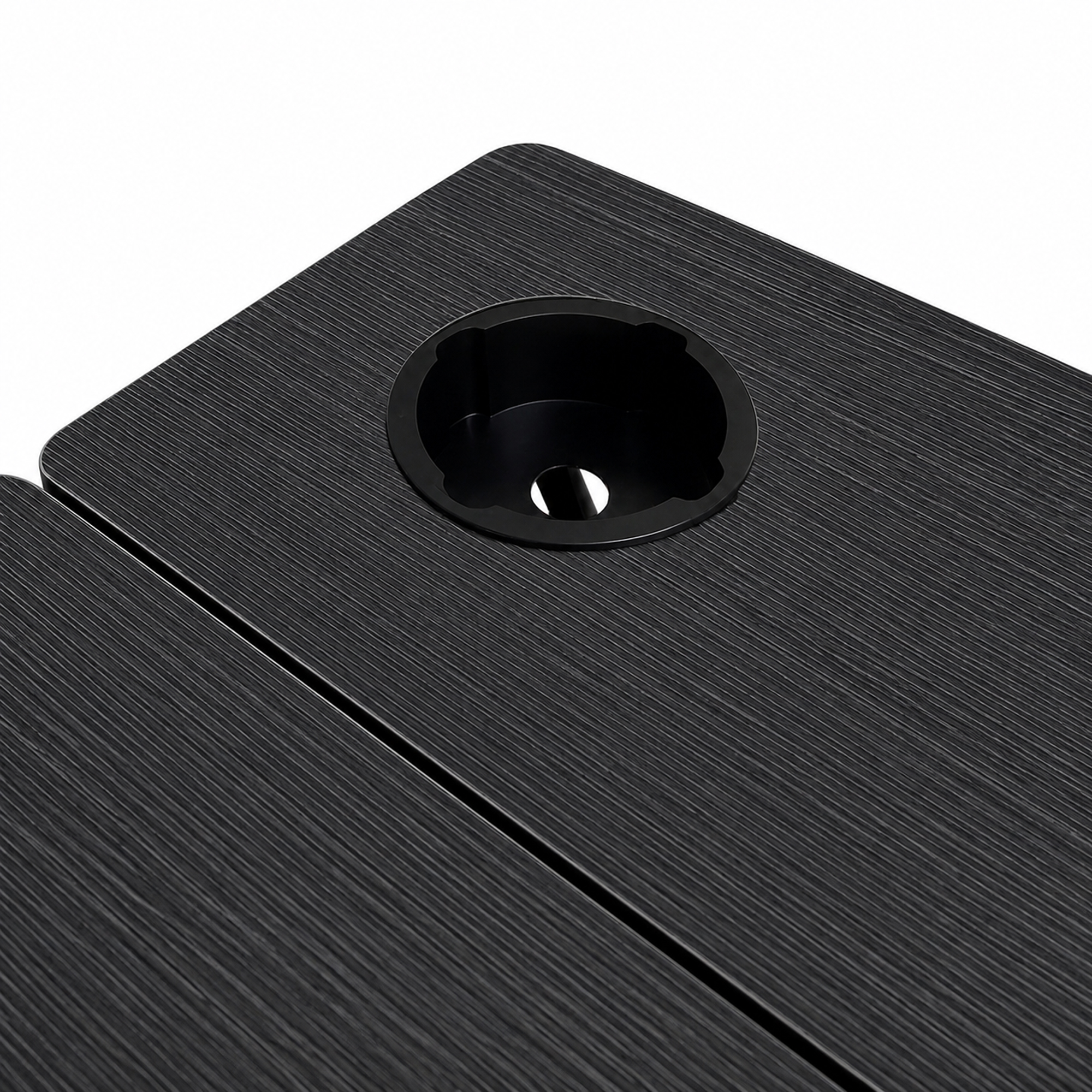 Primer plano de una superficie de mesa negra texturizada con un pasacables redondo negro.