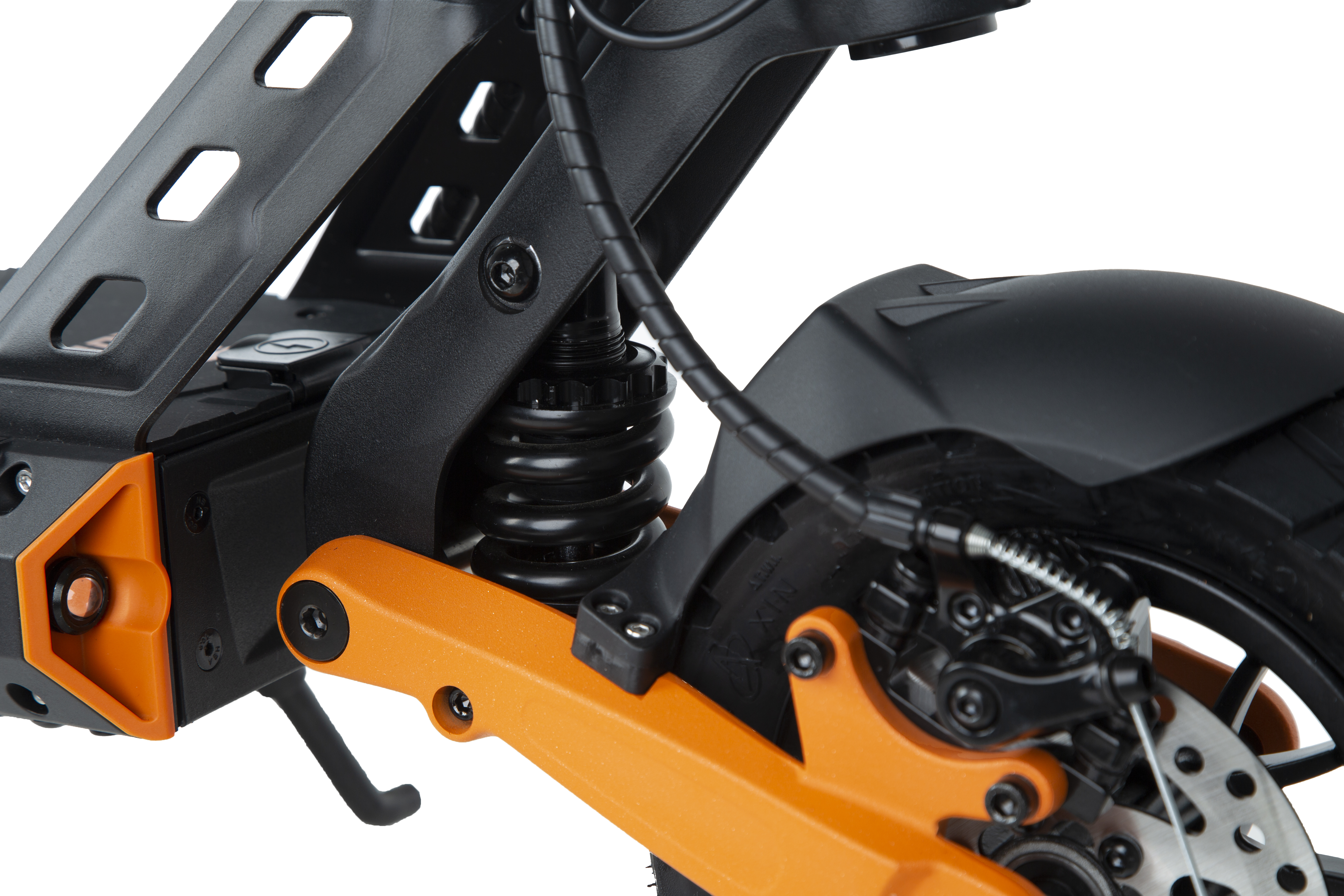 Primer plano de la suspensión negra y naranja y la rueda trasera de un patinete eléctrico sobre fondo blanco.