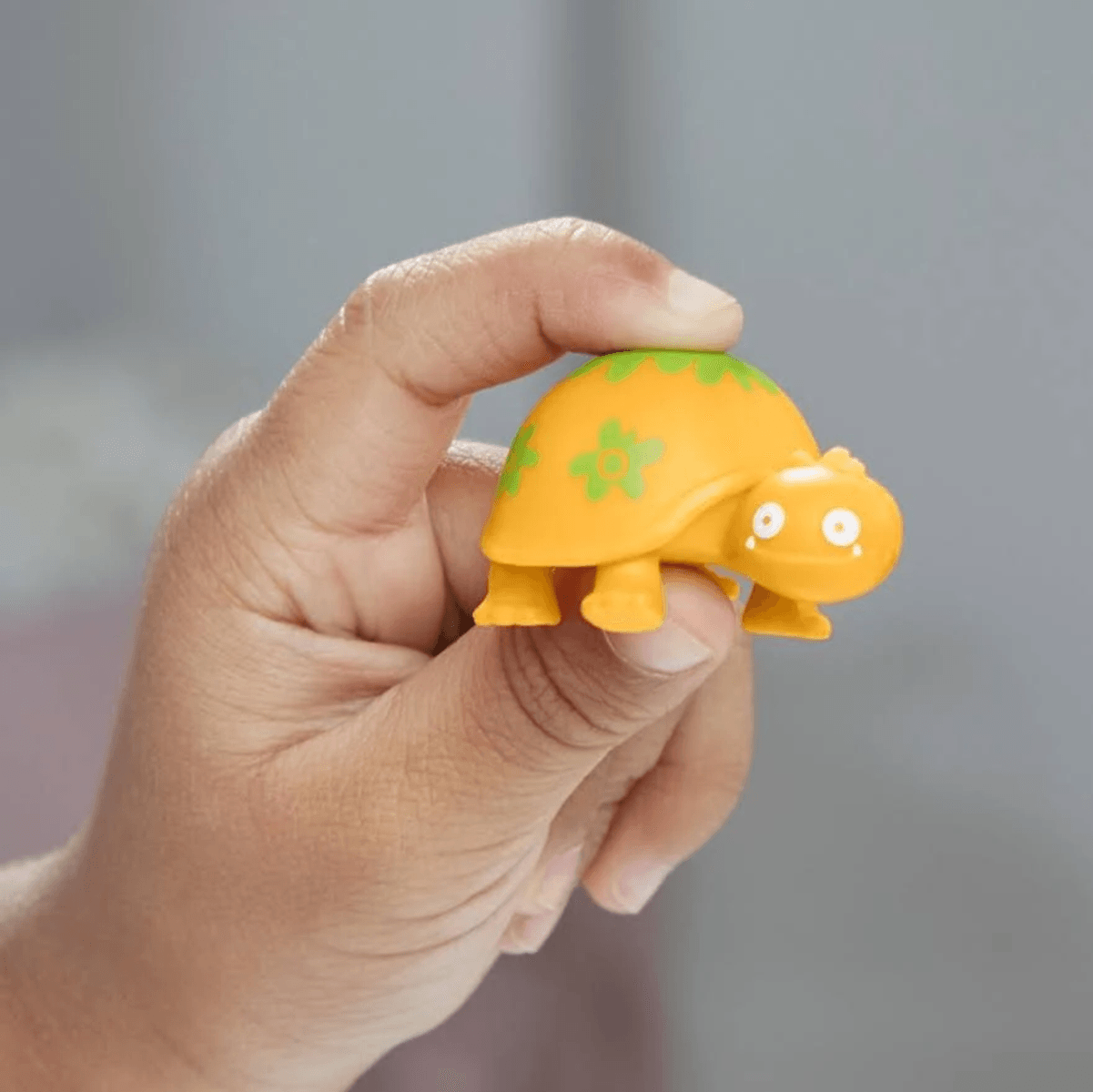 Una mano sostiene una pequeña tortuga de juguete amarilla con un patrón verde en la espalda.