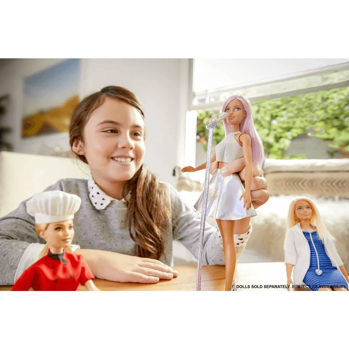 Ein smiling Mädchen spielt mit drei Barbie-Puppen, einer Köchin, einer Sängerin und einer Ärztin.