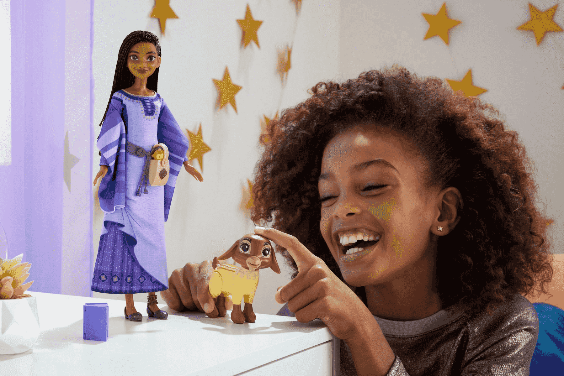 Ein glückliches Mädchen spielt auf einem Tisch mit einer Puppe und einer kleinen Ziegenfigur.