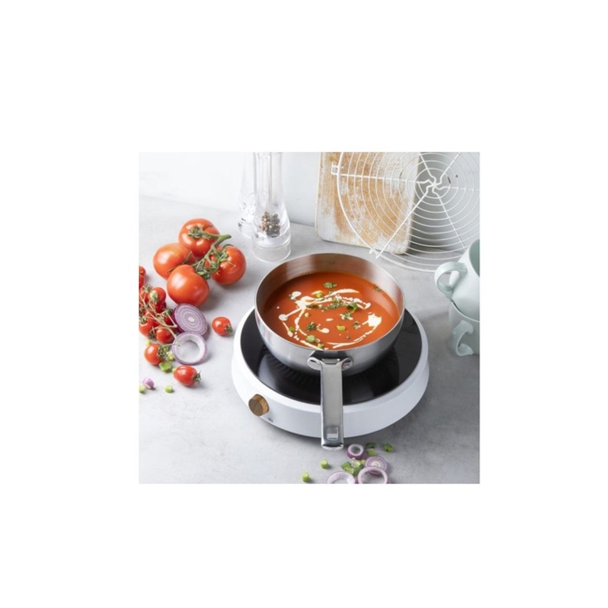 Eine edelstahlpfanne mit tomatensuppe auf einem kochfeld, umgeben von tomaten und zwiebelringen.