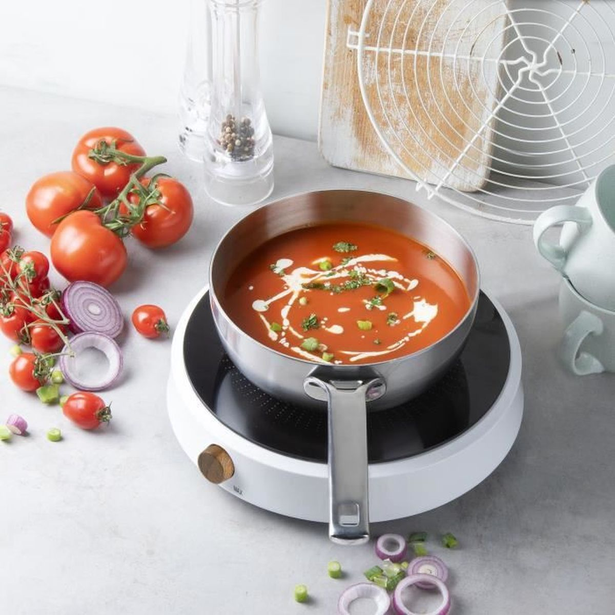 Eine Suppe in einer Pfanne auf einem Herd, umgeben von Tomaten, Zwiebeln und Gewürzen auf der Theke.