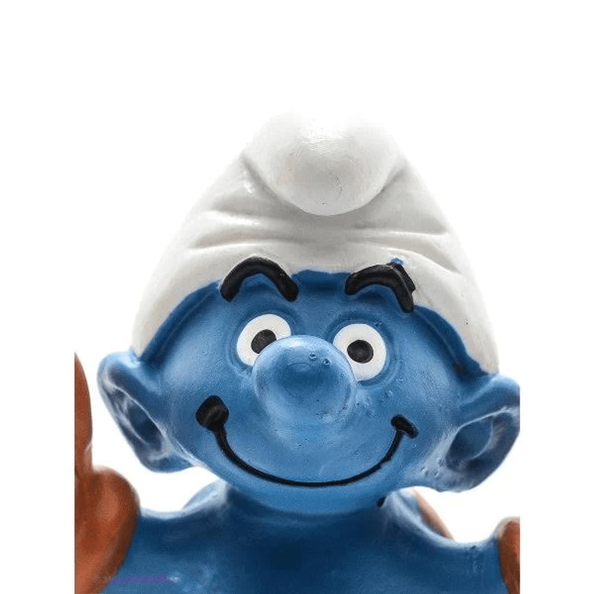 Primer plano de una figura de Pitufo azul con gorro blanco, cara sonriente y nariz redonda sobre fondo blanco.