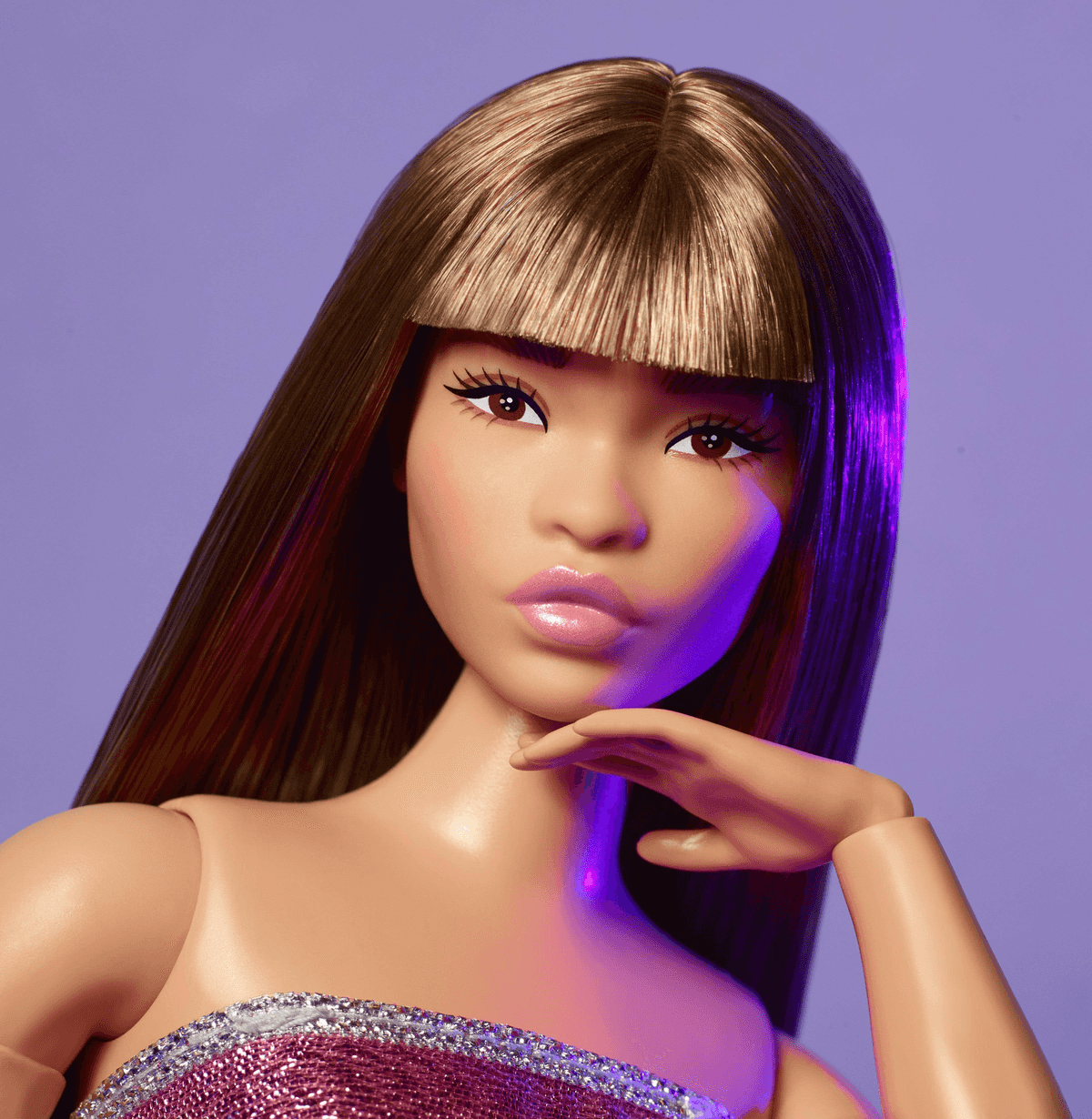 Primo piano di una fashion doll con lunghi capelli castani, frangetta, labbra rosa e top glitterato su sfondo viola.
