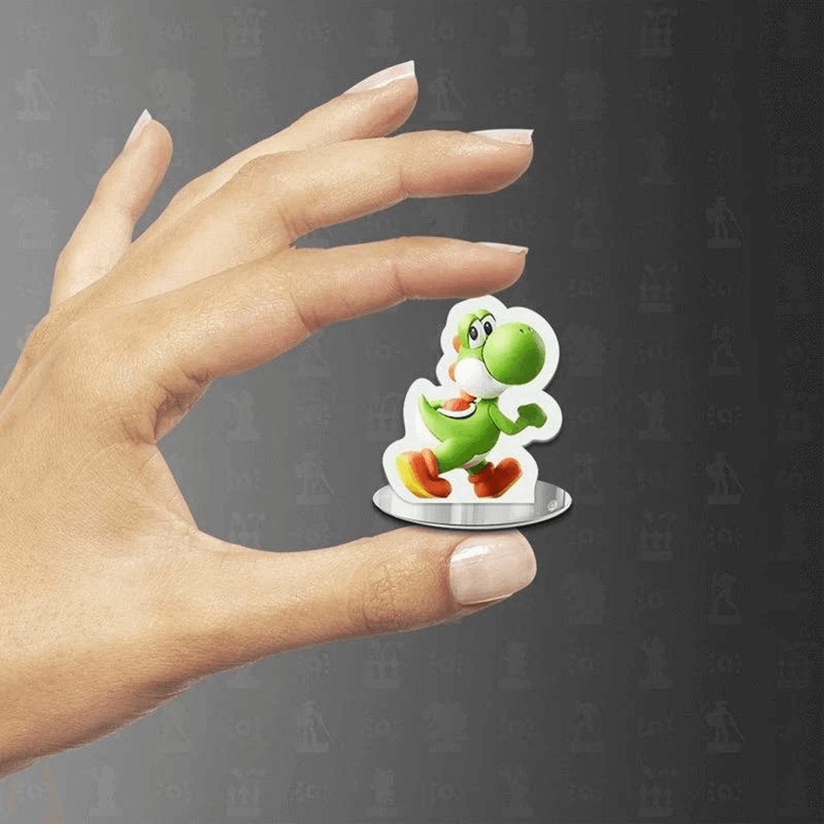 Eine Hand hält eine kleine Yoshi-Spielfigur auf einem runden Sockel vor dunklem Hintergrund.