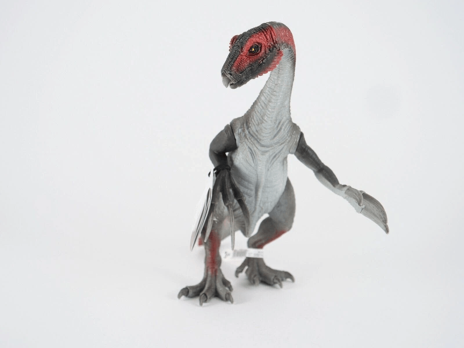 Un dinosauro giocattolo grigio e rosso con artigli lunghi su sfondo bianco.