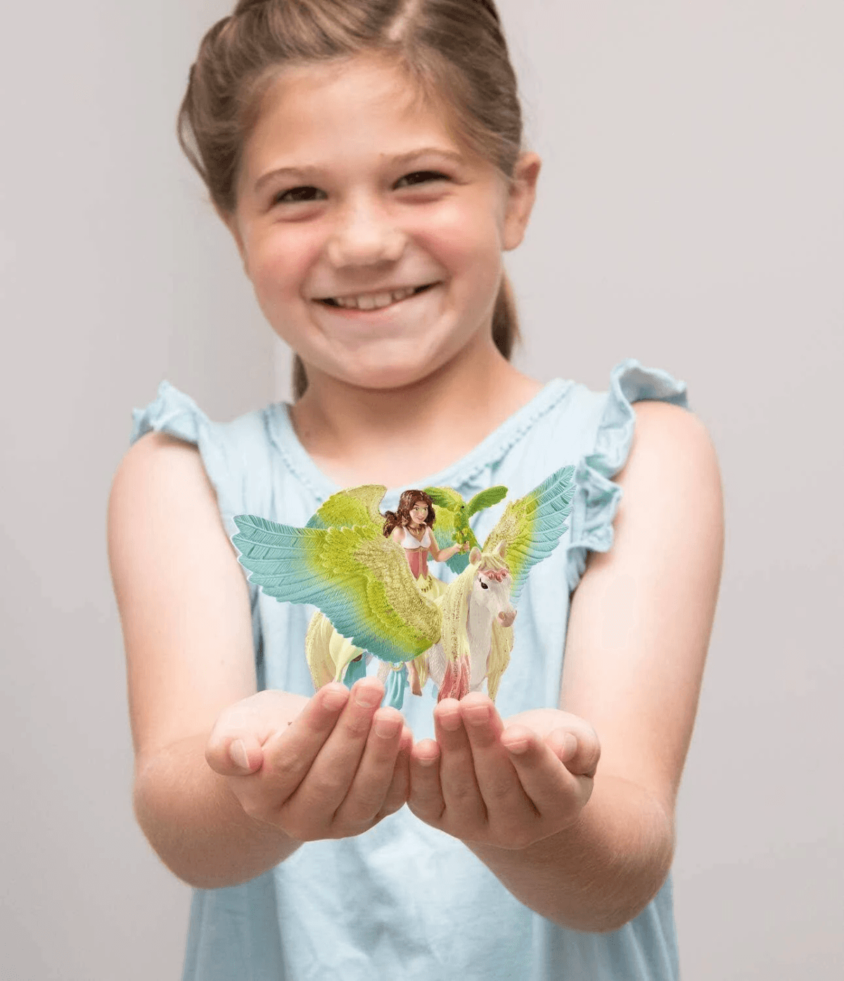 Una bambina felice tiene in mano una statuetta di fata su un unicorno alato.