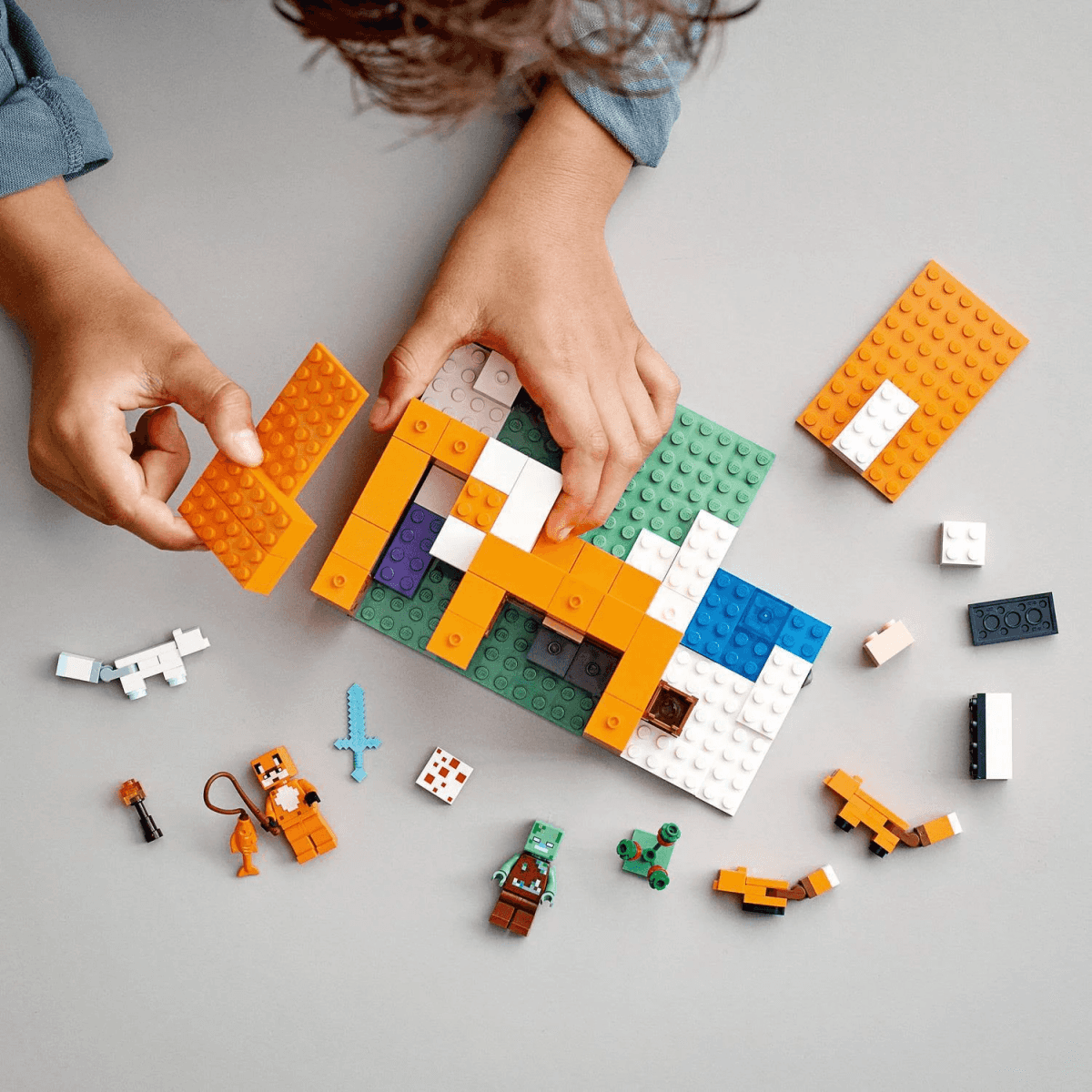 Un bambino assembla un set LEGO Minecraft su un tavolo grigio con le figure.