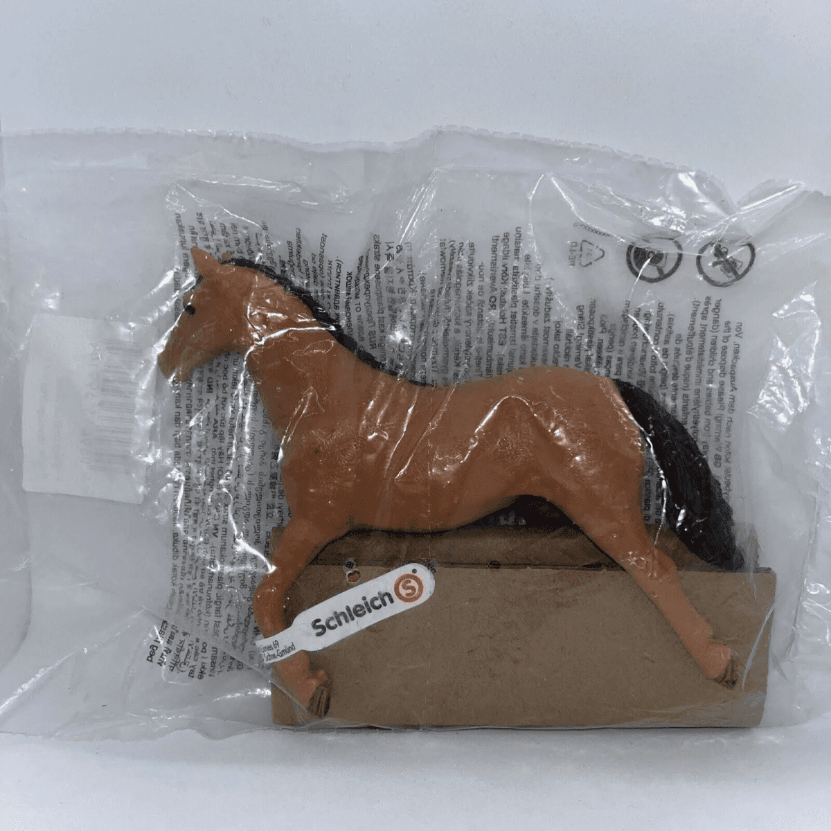 Una figura de caballo marrón de Schleich con crin y cola negras dentro de una bolsa de plástico.