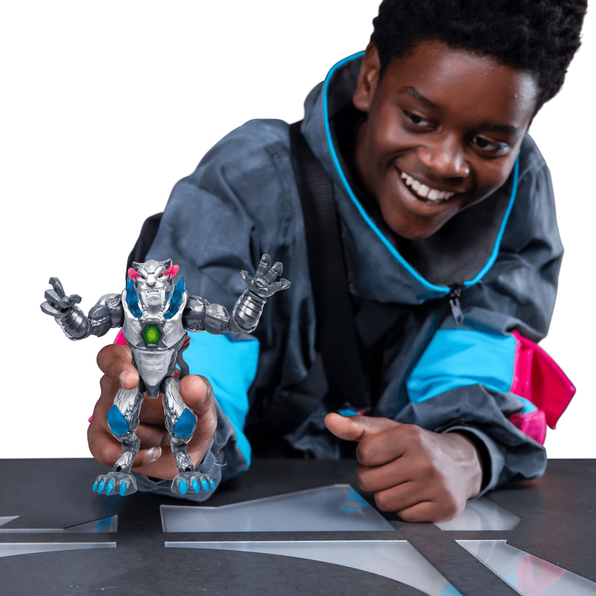 Ein lächelnder Junge in blauer Jacke hält eine silberne Actionfigur mit blauen Details und Leuchtakzenten in den Händen.