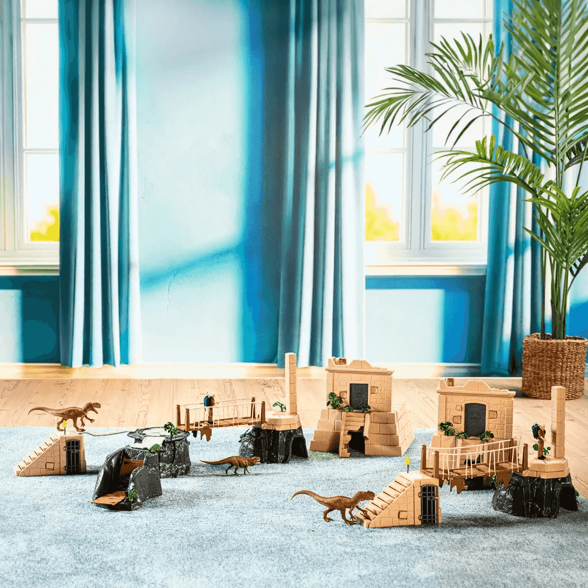Dinosaurier-Spielset auf einem blauen Teppich vor einem großen Fenster mit blauen Vorhängen und einer Zimmerpflanze.