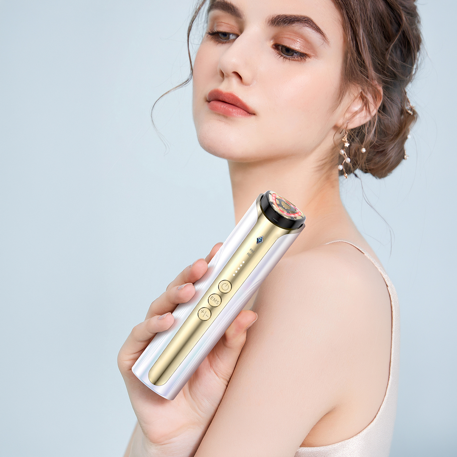 Una mujer sostiene un dispositivo de limpieza facial blanco y dorado contra un fondo azul.