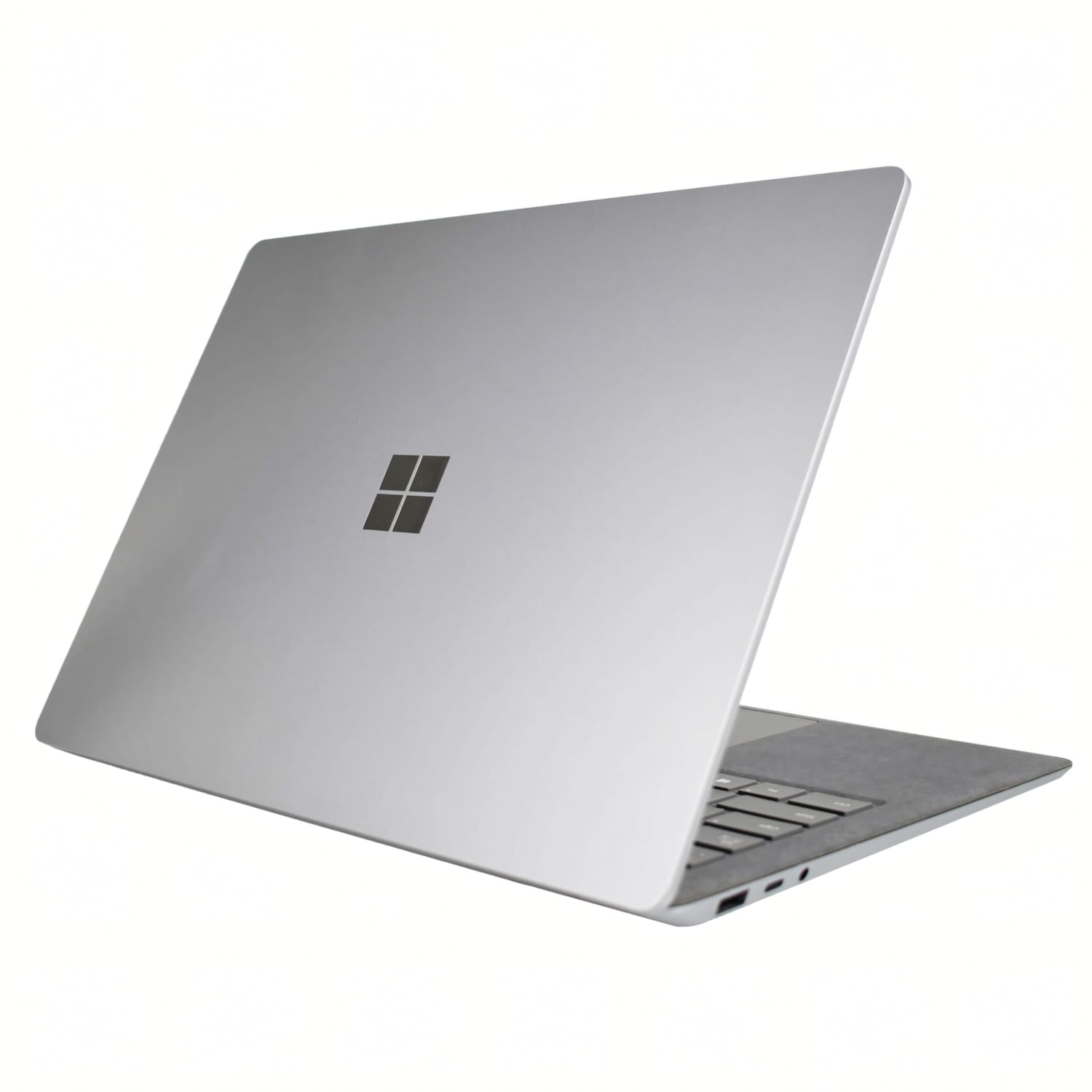 Un ordenador portátil Microsoft plateado está abierto sobre un fondo blanco, mostrando la tapa y el teclado.