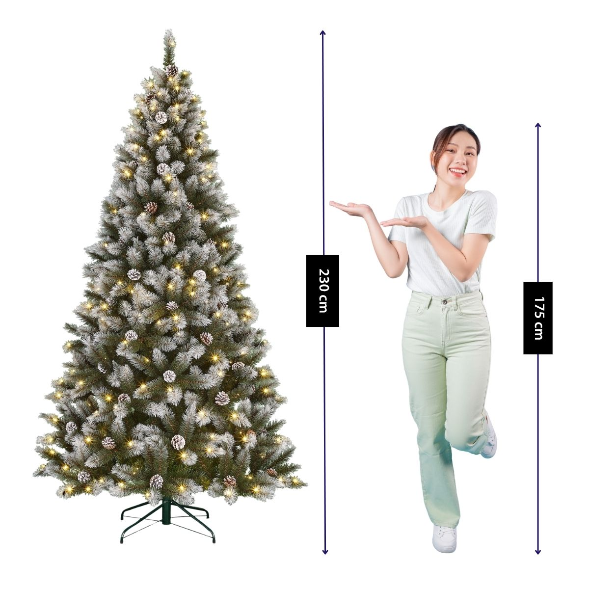 A smiling woman in light clothes gestures toward a tall, frosted artificial Christmas tree with lights.