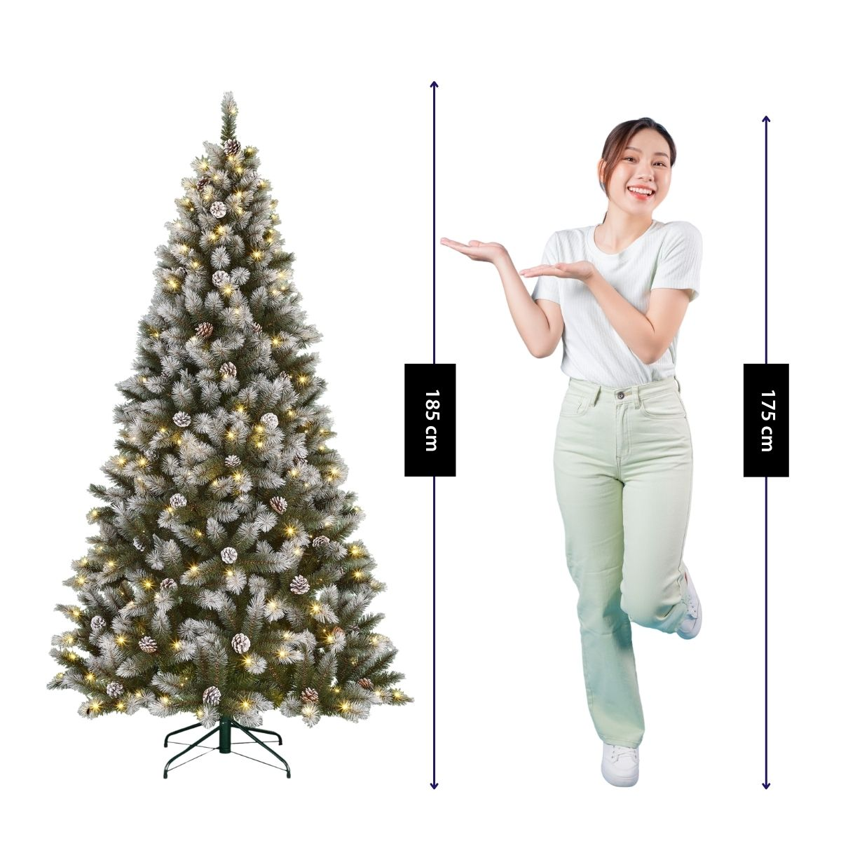 A smiling woman gestures to an artificial snowy Christmas tree with lights and cones, standing 185 cm tall.