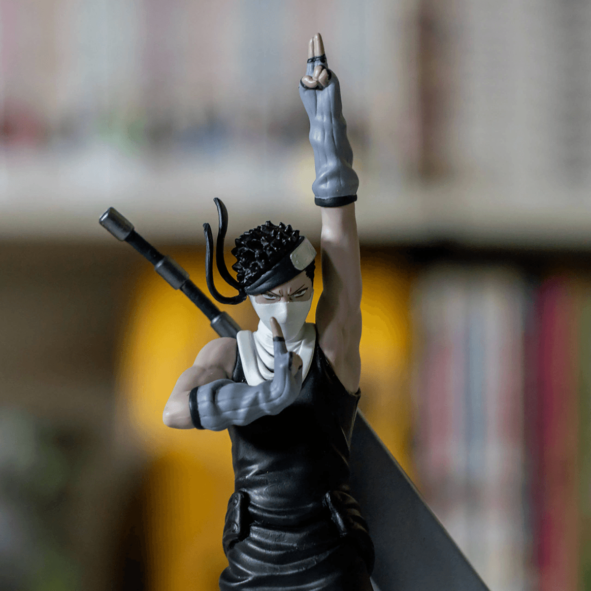 Una figura de anime con ropa negra, máscara y guantes grises hace una seña ninja con las manos.
