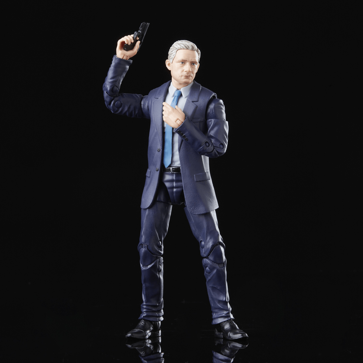 Un action figure in abito blu tiene una pistola e guarda serio su sfondo nero.