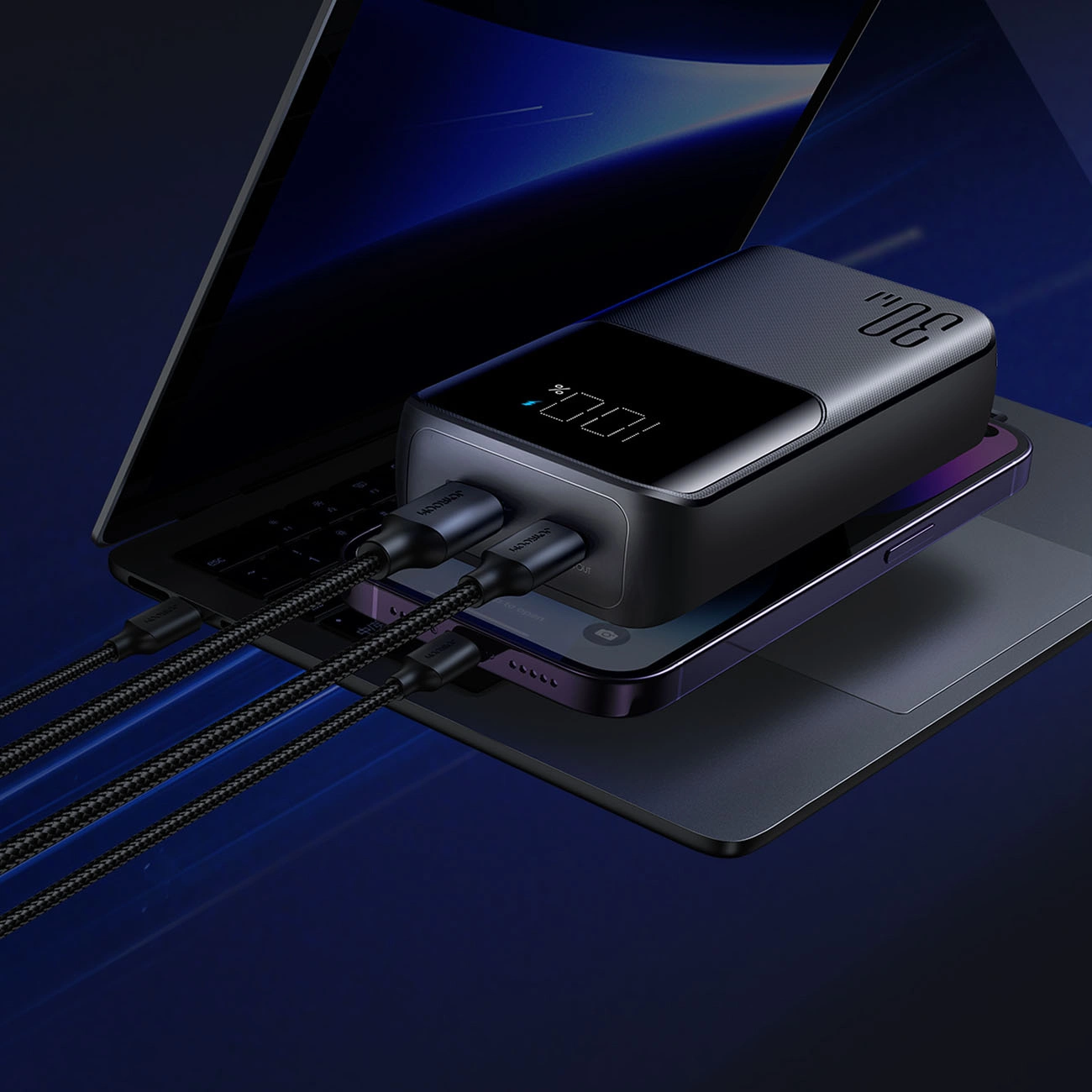 Eine Powerbank mit digitaler Anzeige und angeschlossenen Kabeln liegt auf einem Laptop und Smartphone.