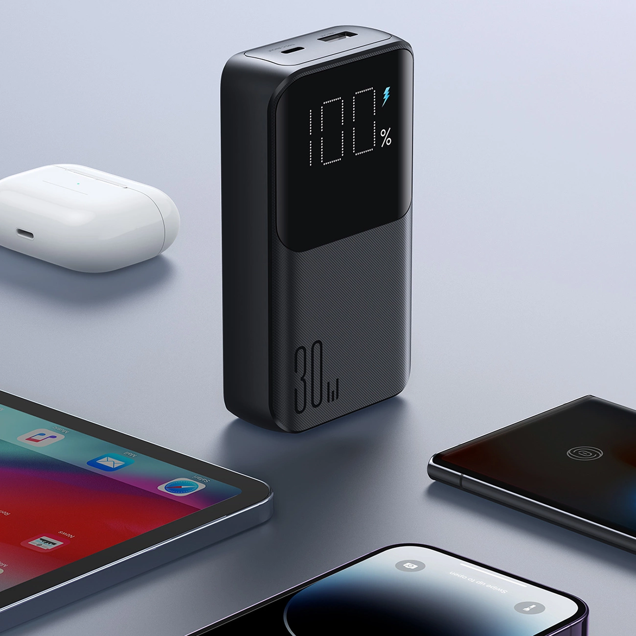 Eine schwarze Powerbank mit LED-Prozentanzeige steht auf einem grauen Tisch, umgeben von Gadgets.