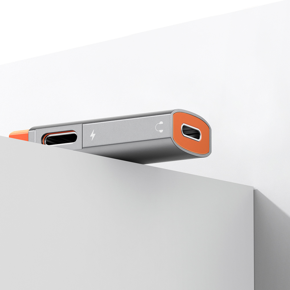Grauer und orangefarbener USB-C-Adapter auf einer weißen Oberfläche mit zwei Anschlüssen und Symbolen.