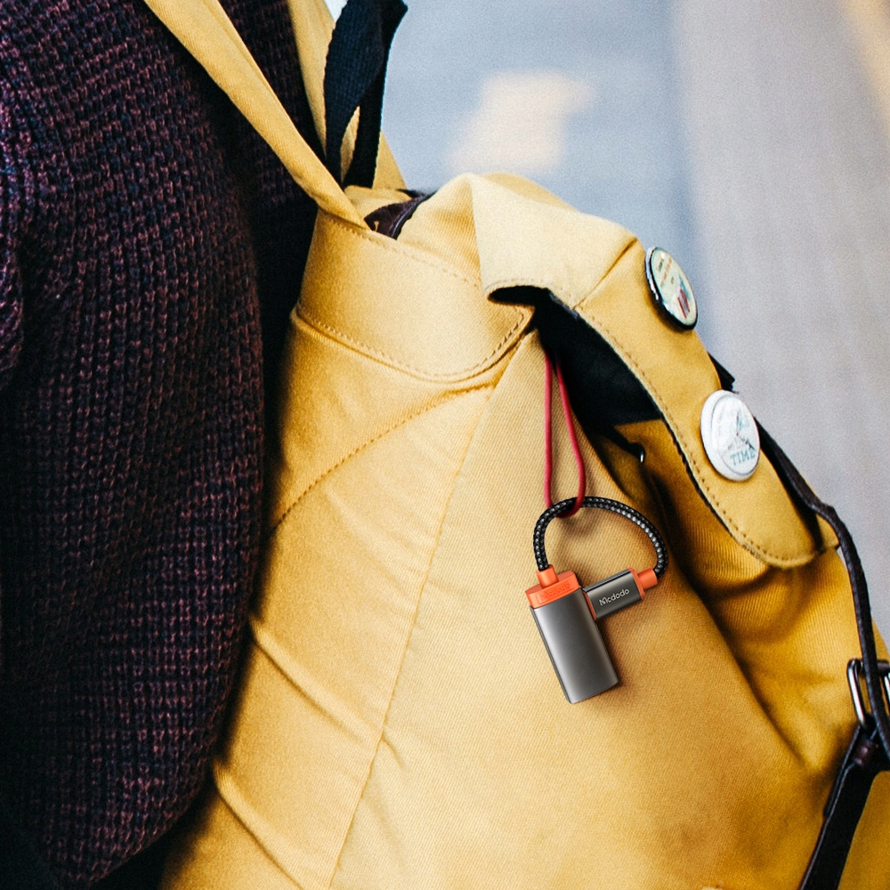 Ein grauer USB-C-Hub mit Kordel hängt an einem gelben Rucksack.