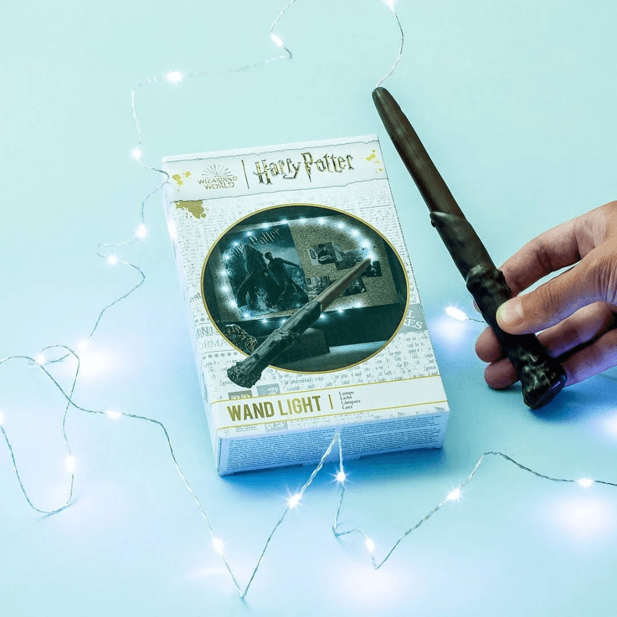 Una mano sostiene una varita junto a la caja de la lámpara varita de Harry Potter, rodeada de luces.