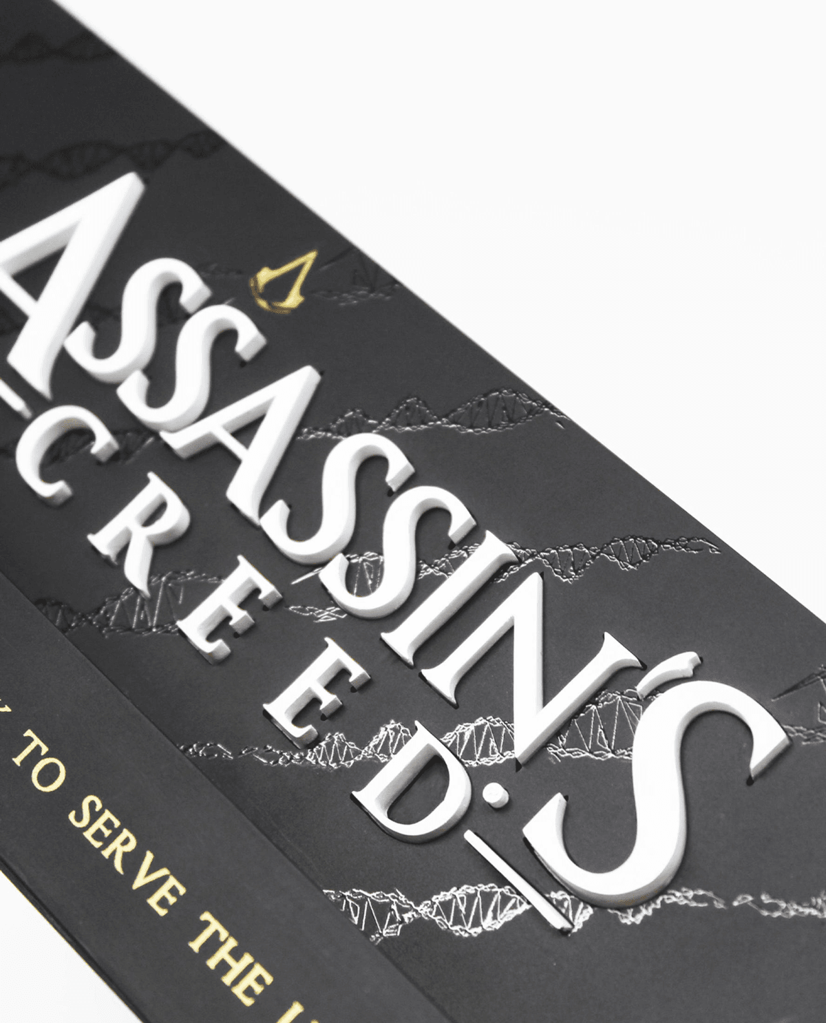 Nahaufnahme einer schwarzen Assassin's Creed Schachtel mit erhabener weißer Schrift und goldenem Logo.