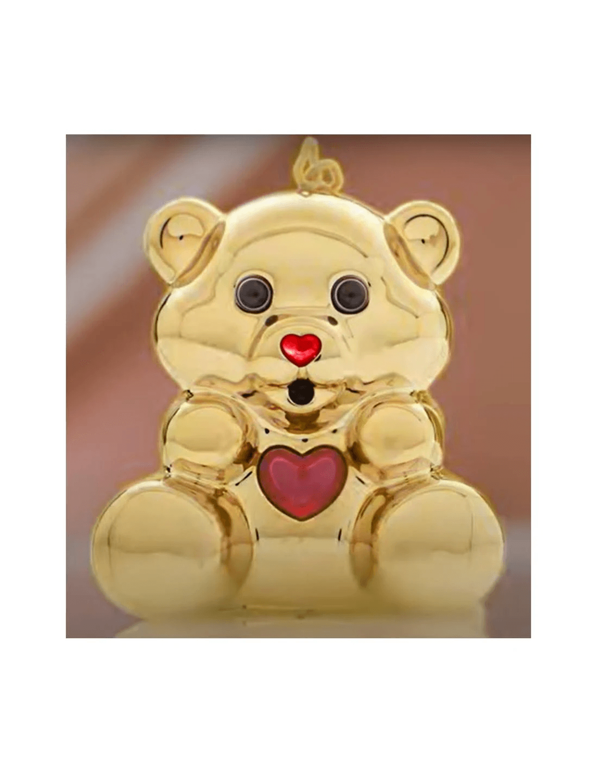 Una brillante figura de oso de peluche dorado con nariz y pecho de corazón rojo, ojos negros y boca abierta.