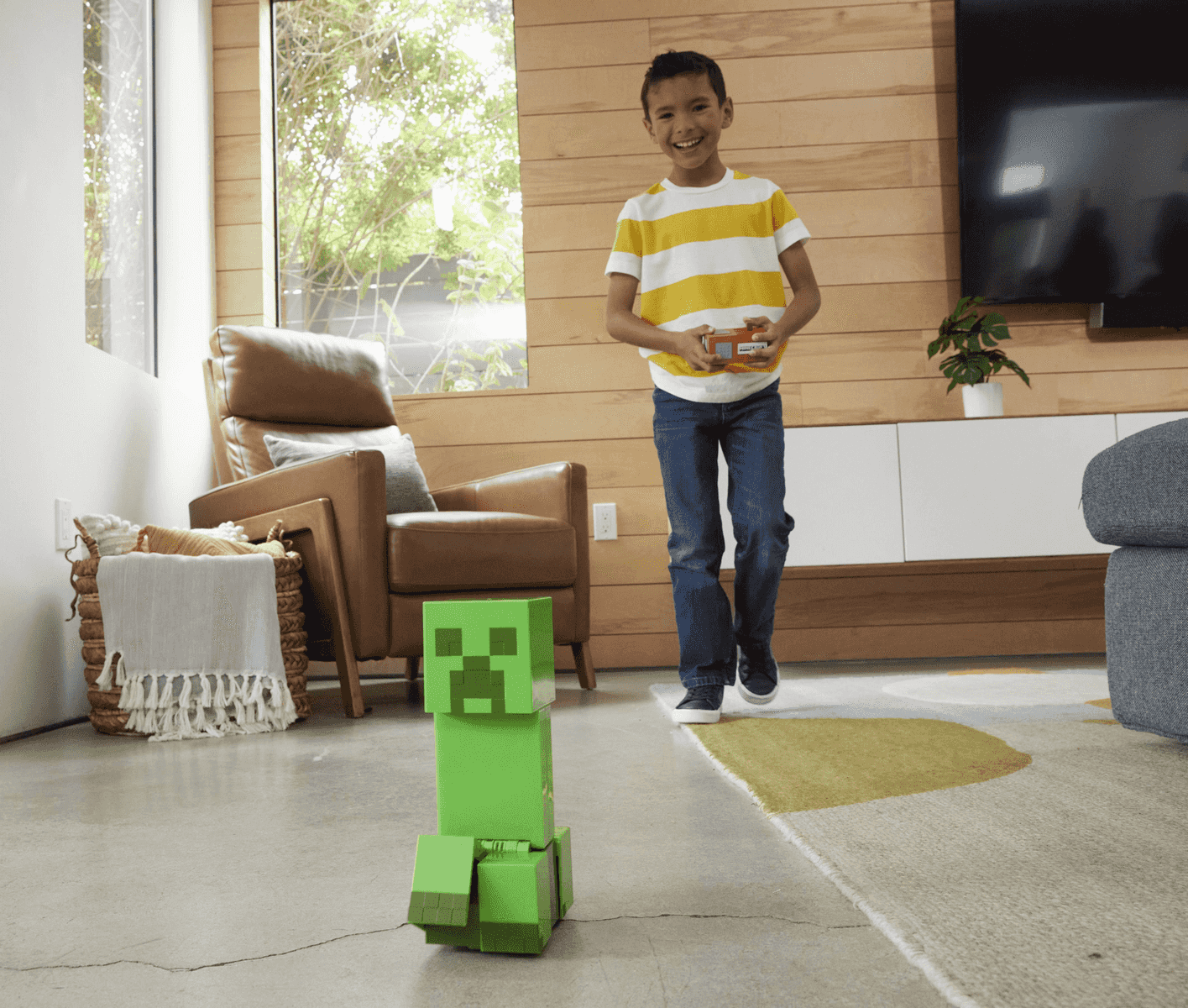 Ein Junge lächelt, während er einen ferngesteuerten grünen Minecraft-Creeper-Roboter bedient.