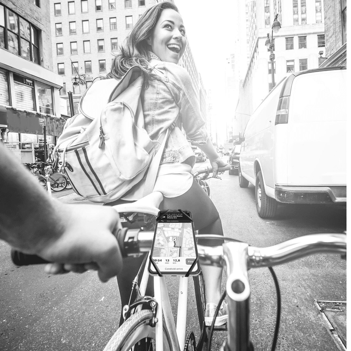 Foto en blanco y negro de una mujer montando en bicicleta en una ciudad con un soporte para teléfono.