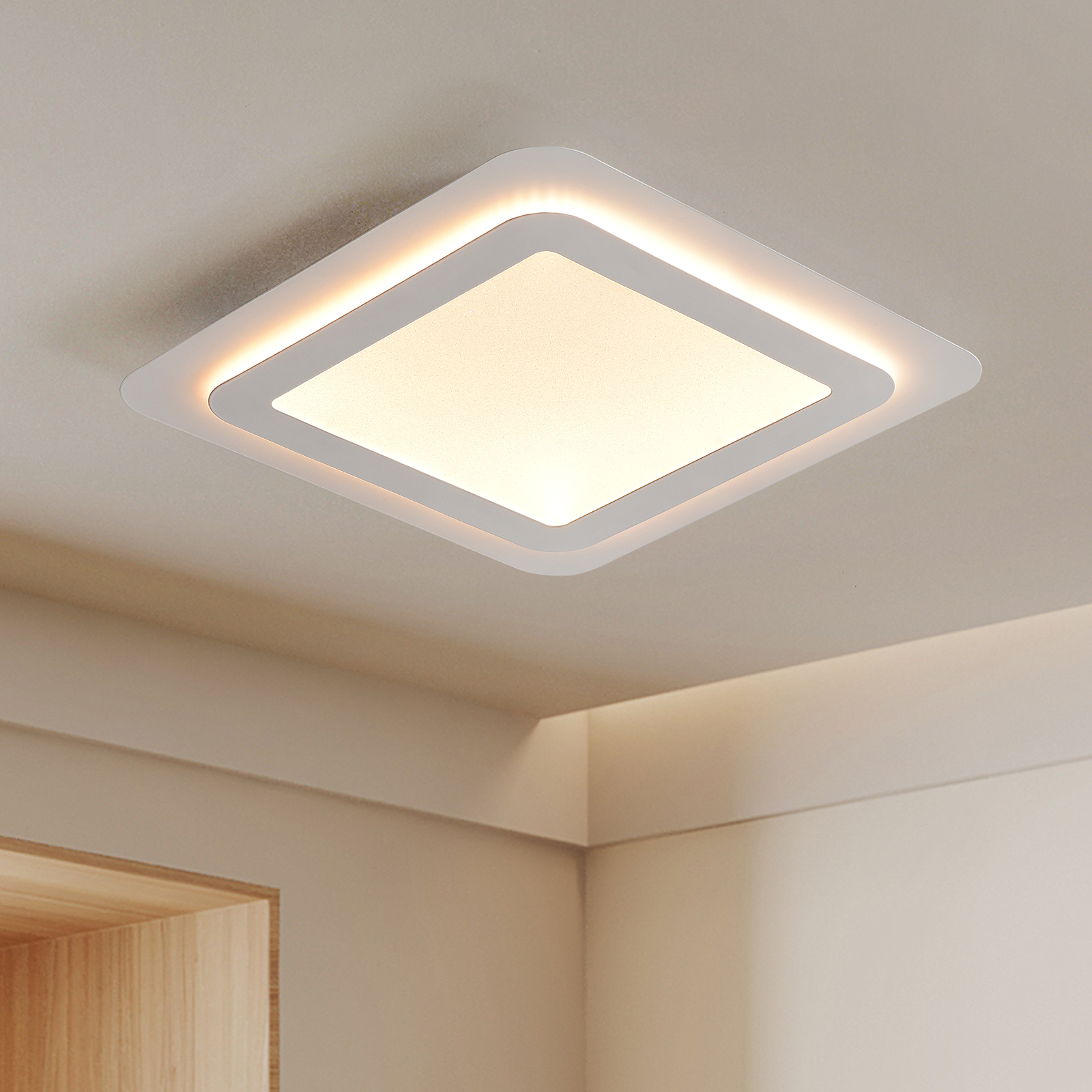 Eine weiße, quadratische LED-Deckenleuchte leuchtet an einer hellen Zimmerdecke.