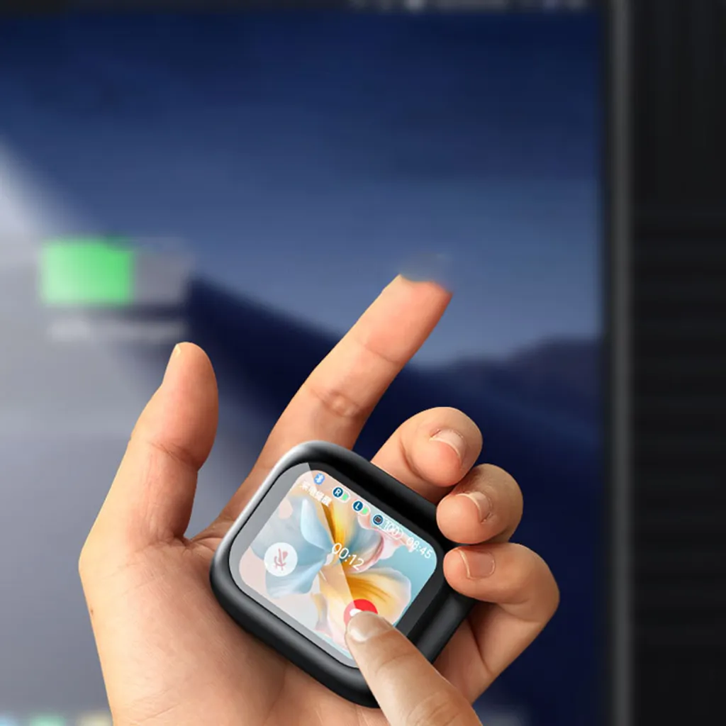 Eine Hand hält eine kleine, quadratische Smartwatch mit buntem Display vor einem unscharfen Monitor.