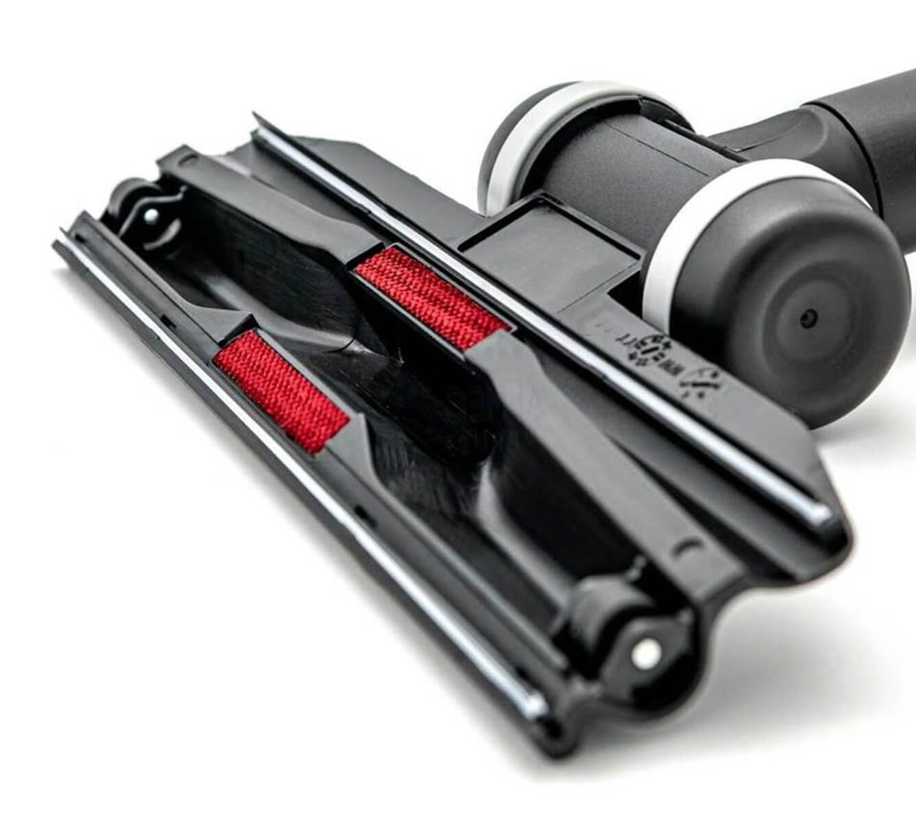 Dessous d'une brosse d'aspirateur noire avec des bandes rouges et des roulettes sur fond blanc.