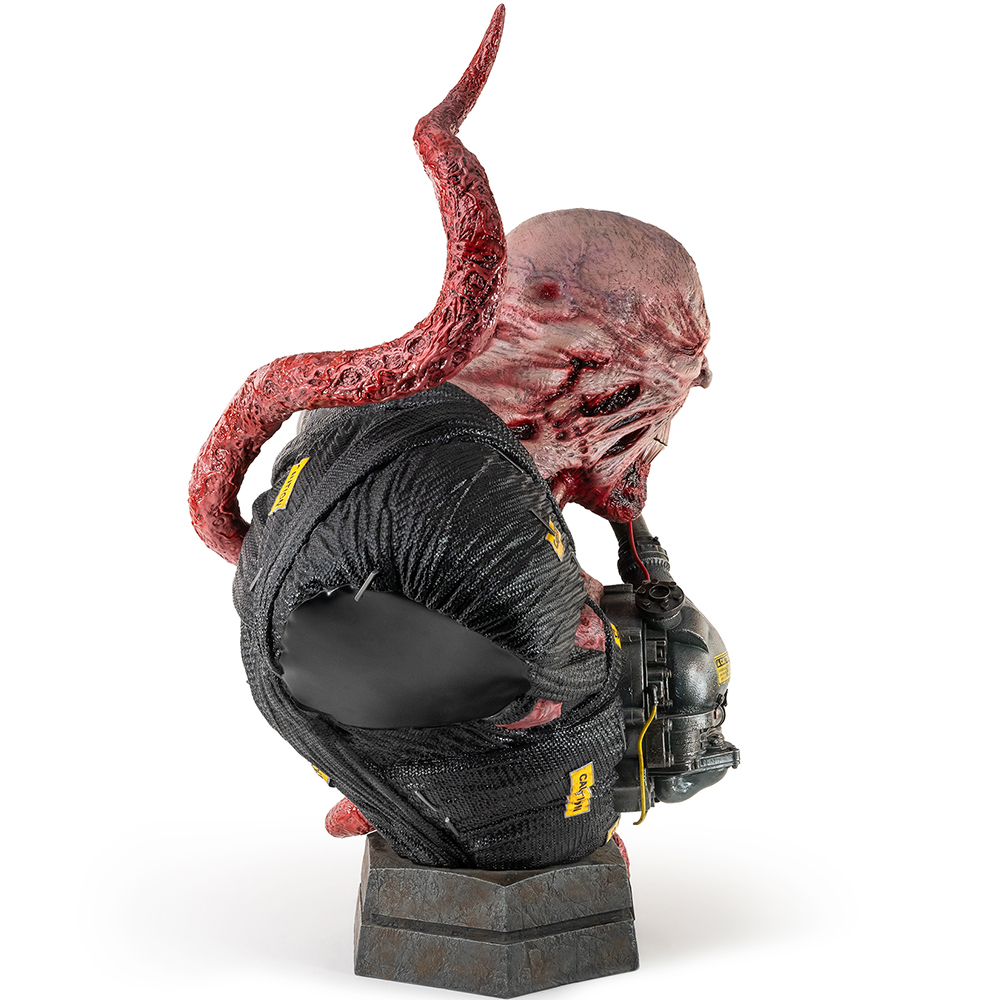 Skulptur einer Kreatur mit Tentakel, der aus dem Rücken ragt, und schwarzer Kleidung auf einem Sockel.