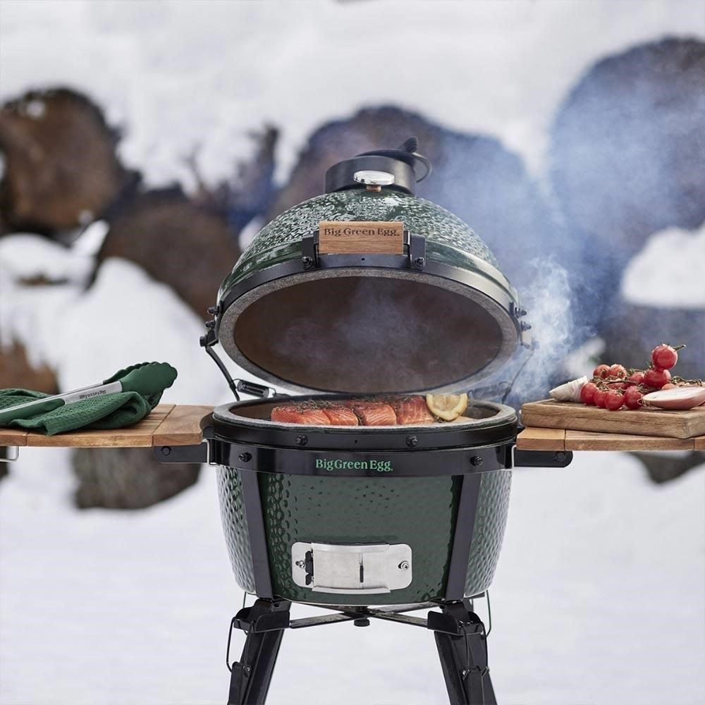 Karlı kış arka planında, dışarıda dumanla somon pişiren yeşil Big Green Egg mangal.