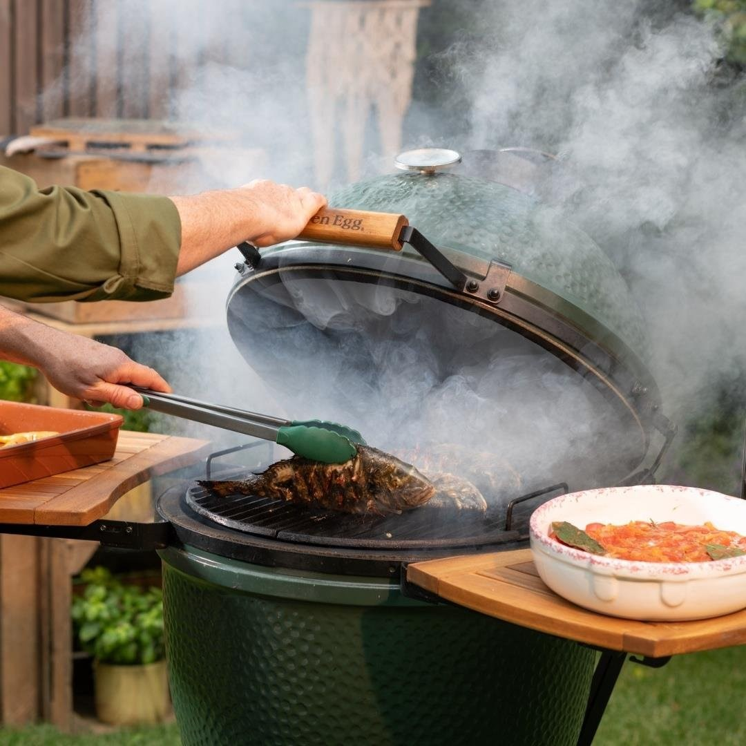 Yeşil yumurta barbeküde yükselen dumanla balık ızgara yapan kişi.