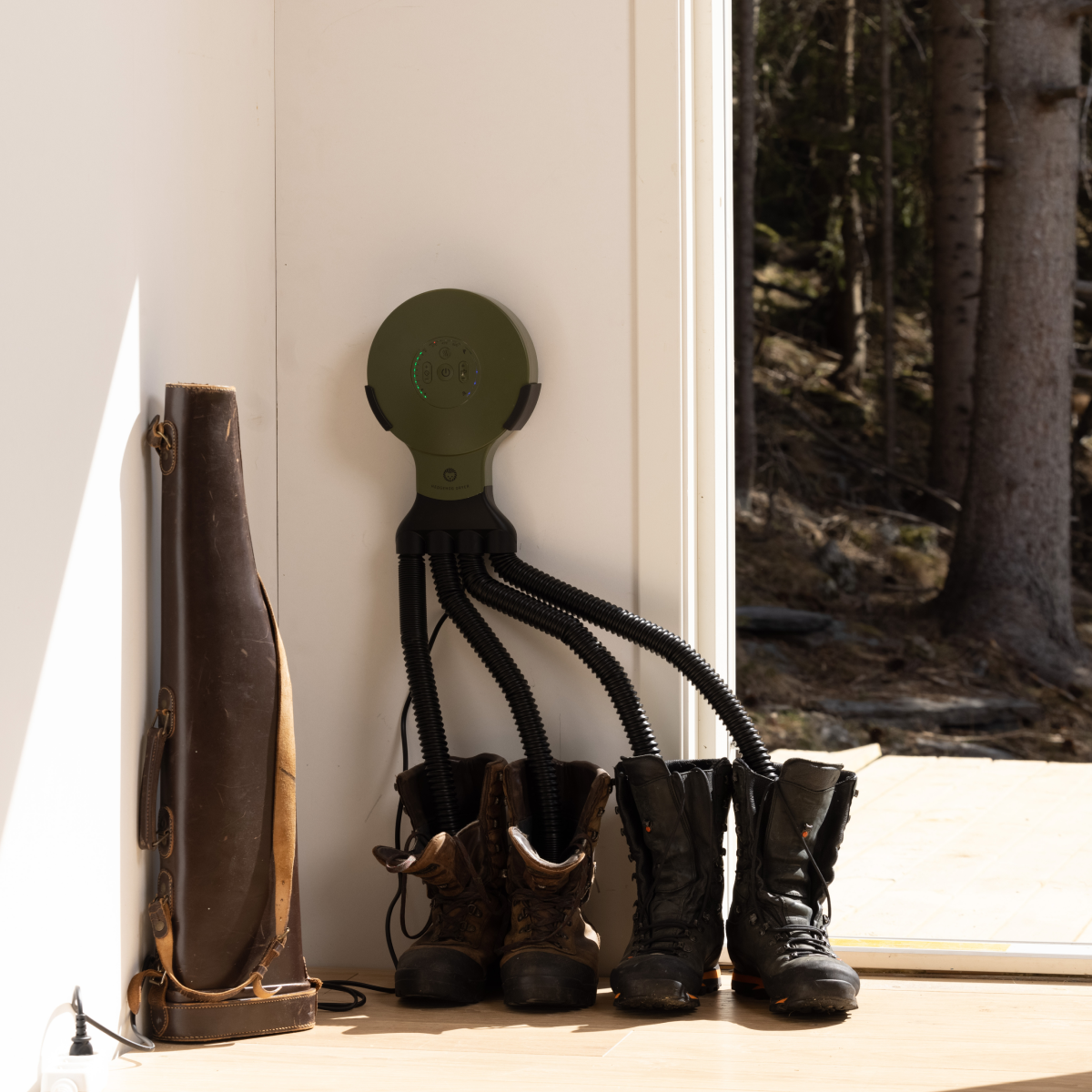 Ein Schuhtrockner mit vier Schläuchen an einer Wand trocknet Stiefel, daneben steht ein Ledertasche.