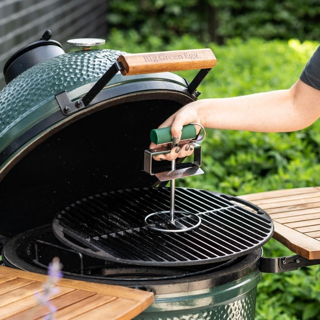 Bir el, açık yeşil renkli Big Green Egg mangalın üzerinde bir ızgara kaldırma aleti tutuyor.