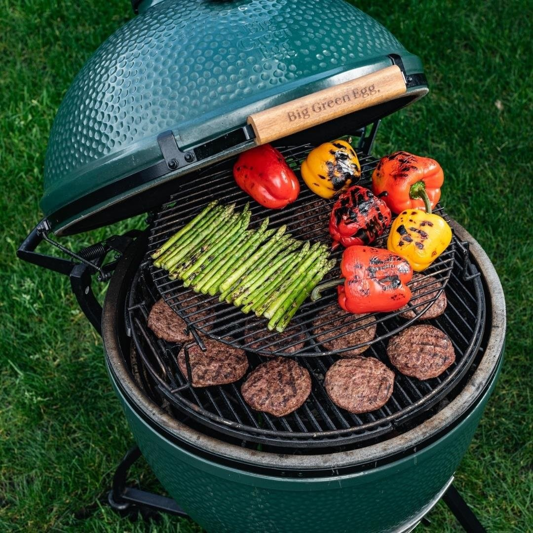 Alt ızgarada köfteler, üst ızgarada kuşkonmaz ve biberler bulunan yeşil seramik barbekü.