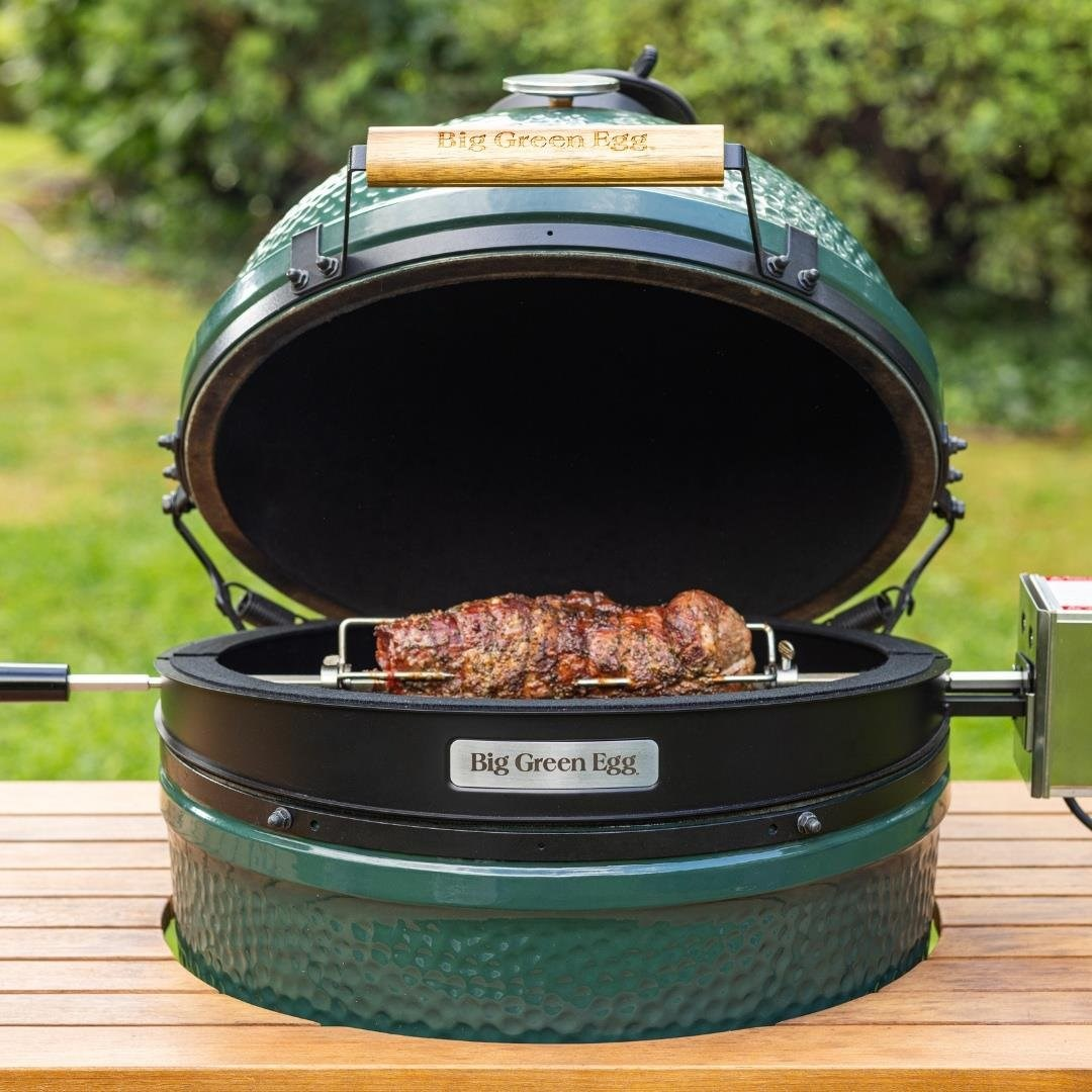 Ahşap masa üzerinde açık yeşil Big Green Egg ızgara ve şişte dönen bir parça et.
