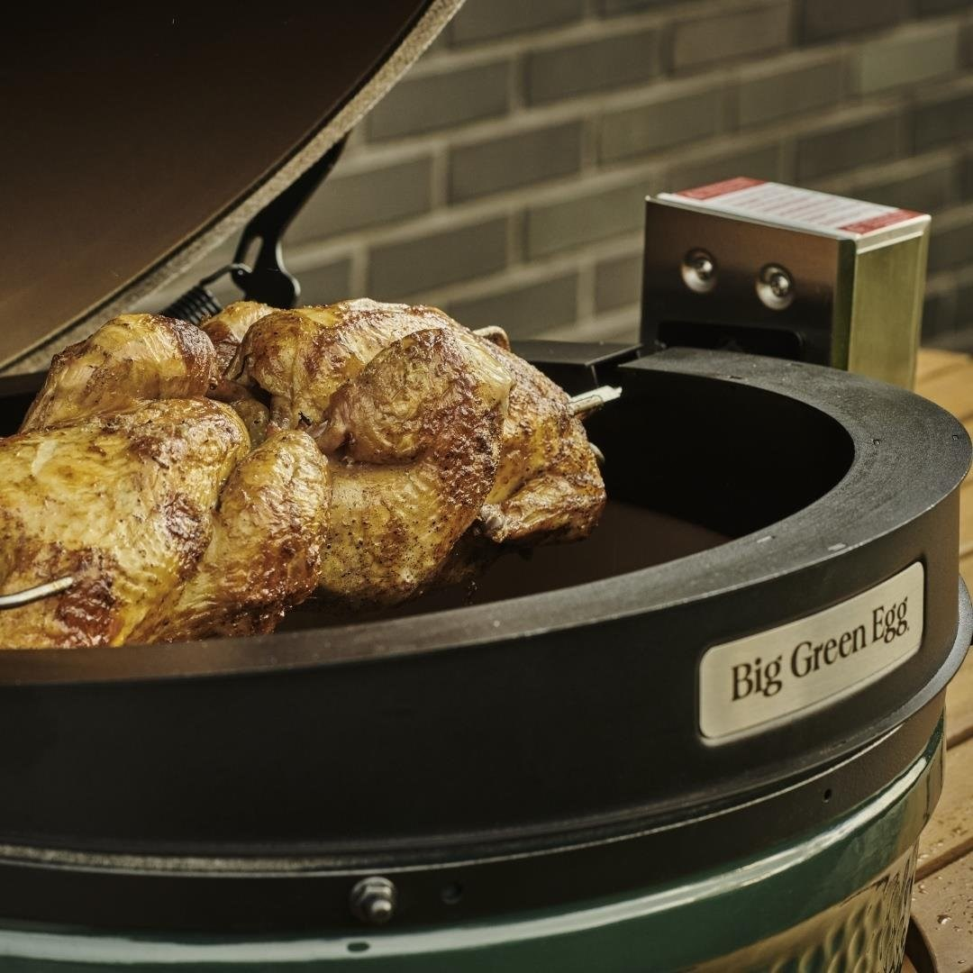 Tuğla arka plan önündeki açık bir Big Green Egg mangalında şişte dönen bütün bir tavuk.
