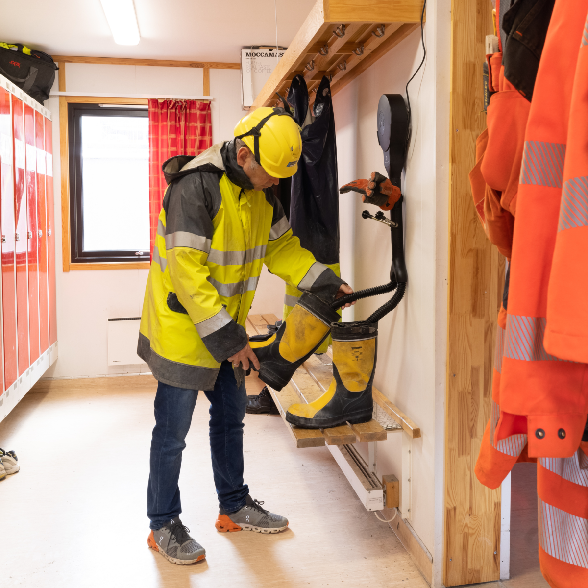 Ein Arbeiter in gelber Sicherheitsjacke und Helm nutzt einen Stiefeltrockner.